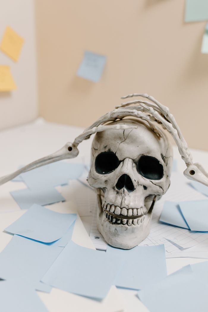 Skeleton skull with hands surrounded by sticky notes on a desk, creating a humorous scene.